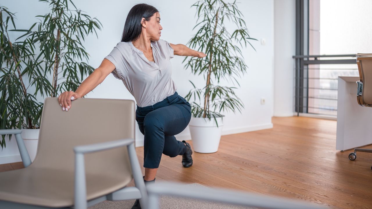 Woman holds back of office chair, twists and lunges