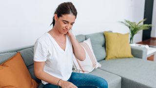 Woman sits on couch holding her neck