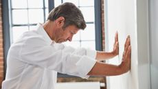 Man in white shirt presses his palms into a wall