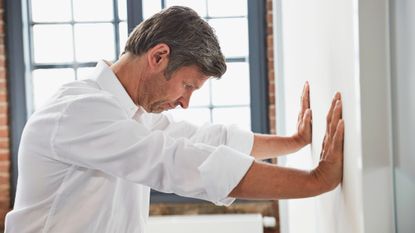 Man in white shirt presses his palms into a wall