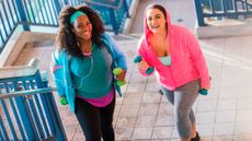 Two women walking up stairs outside holding neoprene dumbbells