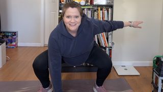 Jennifer Rizzuto exercises at home. She is in a deep squat on a yoga mat, with one hand on the floor and the other held out to the side for balance.