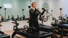 Woman exercising on Lagree Megaformer machine. She kneels on the platform and holds D handles connected to cables in front of her with elbows bent