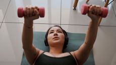 Woman lying on tiled floor pressing dumbbells above her