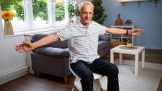 man sat on a chair in a living room setting facing the camera with his eyes closed and arms out to the sides at shoulder height. 