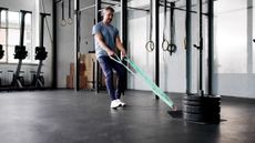 Man in gym walking backward holding straps attached to sled with four weight plates on it