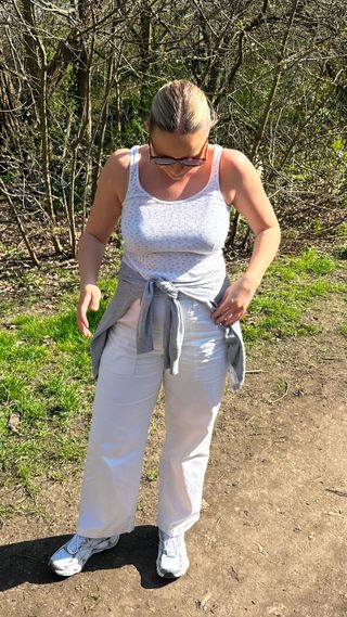 Woman wearing white trainers, white jeans and white tank top and sunglasses in a park, looking at her feet
