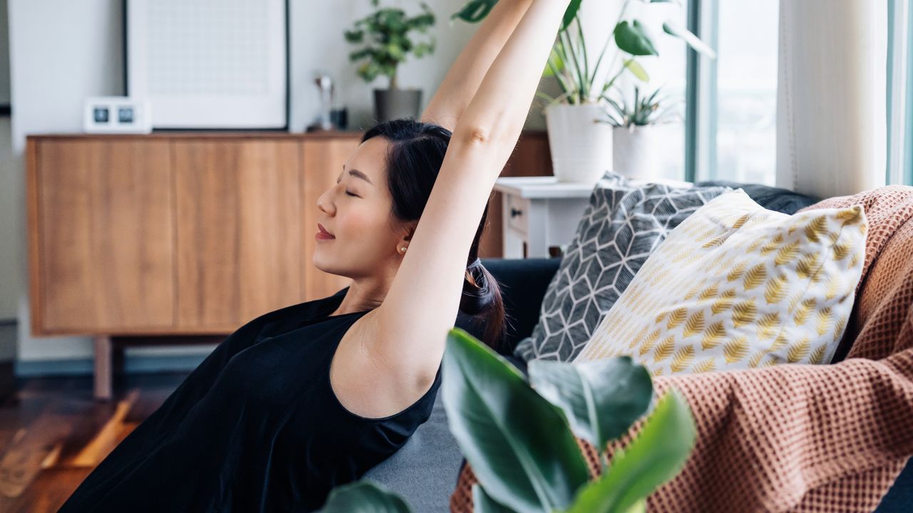 Woman leans back on couch and stretches her arms over her head