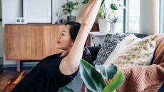Woman leans back on couch and stretches her arms over her head